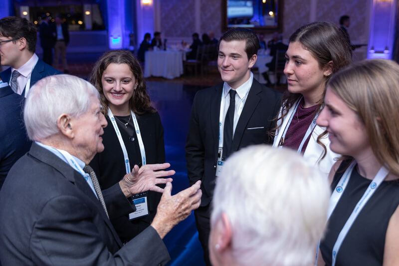 An older man speaking animatedly to a group of young adults.